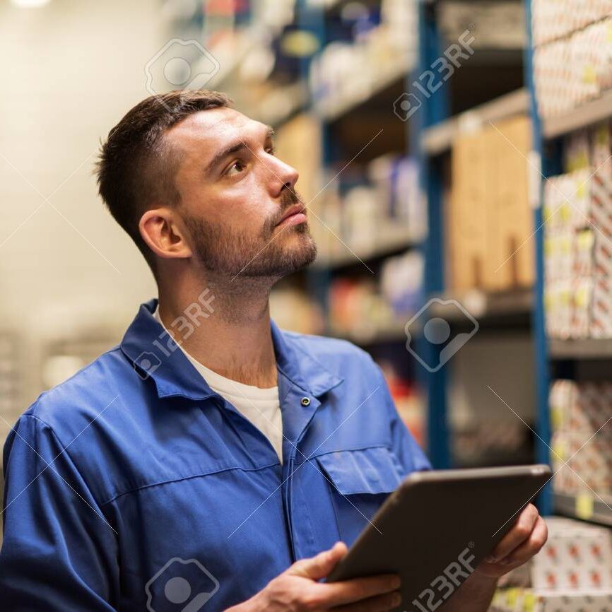 car service, repair, maintenance and people concept - auto mechanic man or smith with tablet pc computer looking for spares at workshop or warehouse